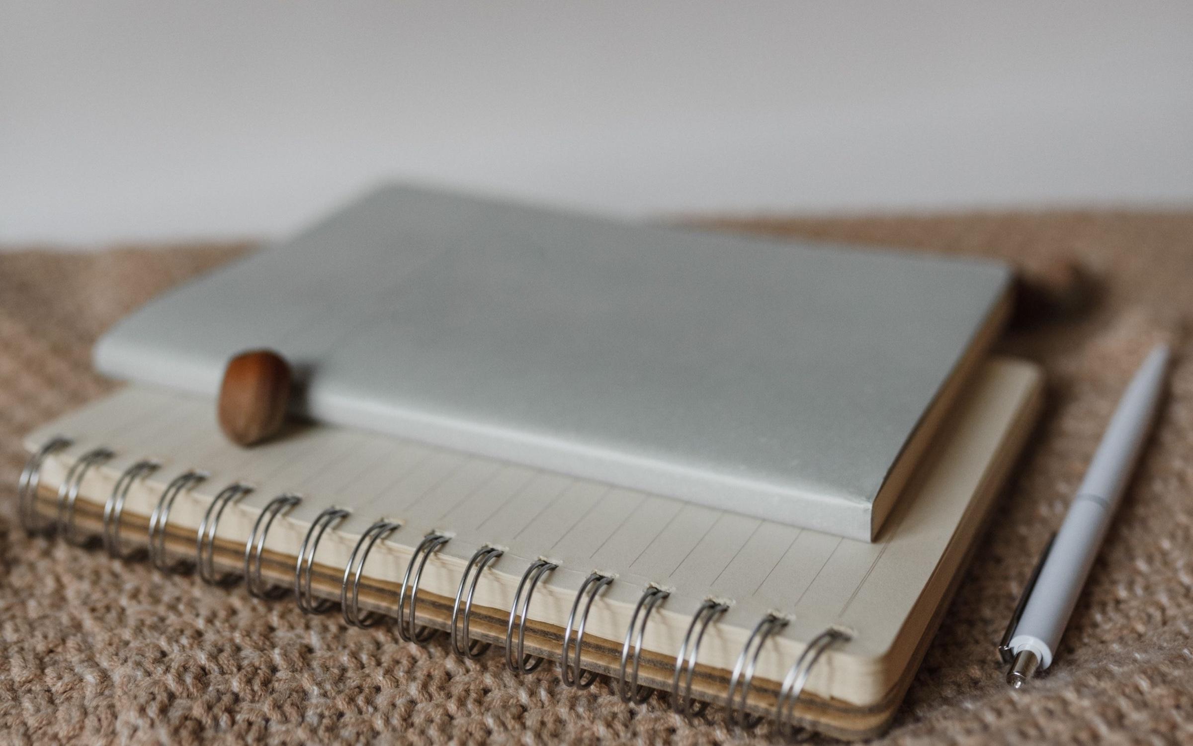 Des cahiers et un stylo posés sur une maille beige