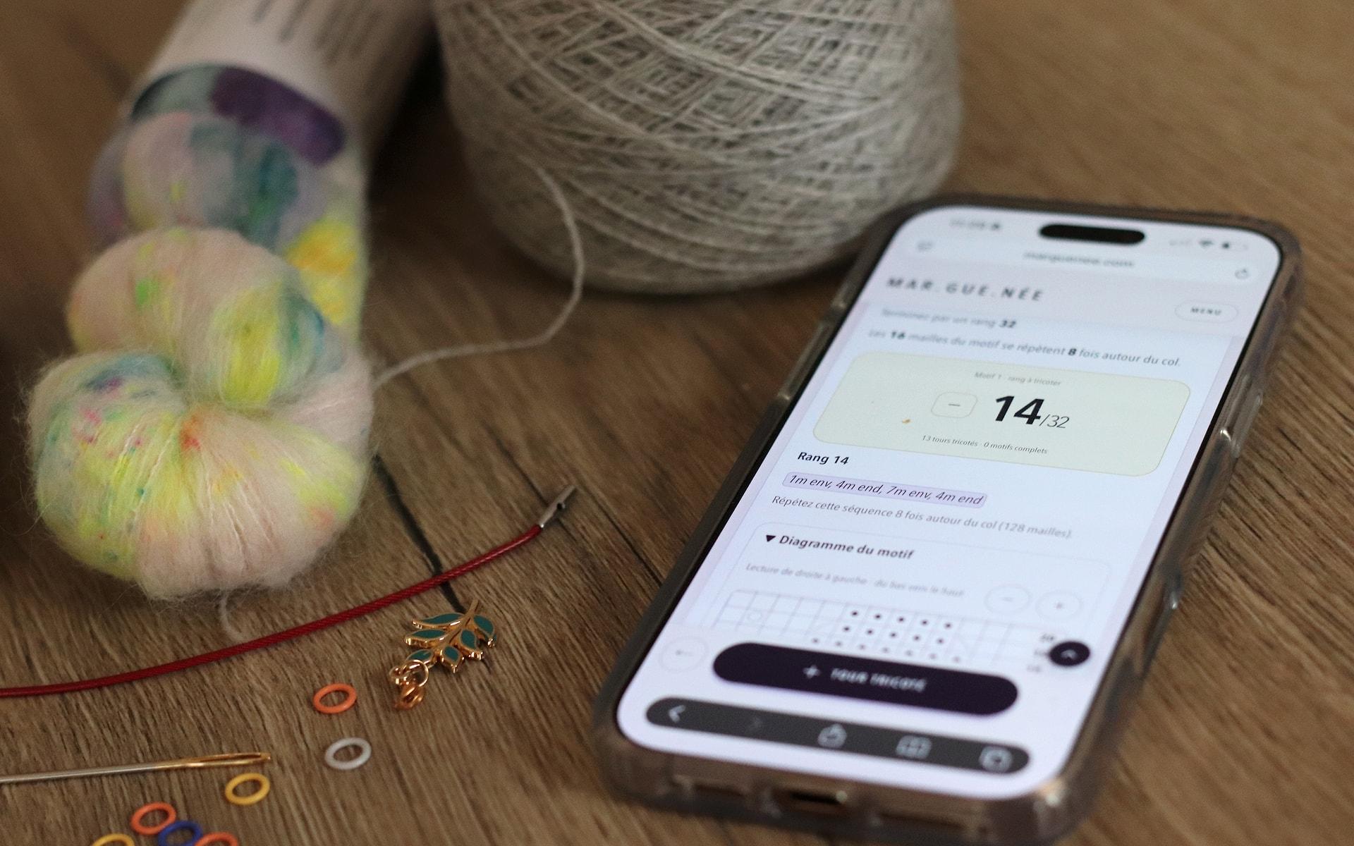 A phone displays the interactive Remiremont pattern beside knitting yarn and stitch markers on a wooden table